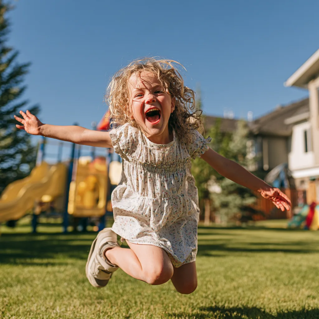 A child jumping with both arms out on a sunny lawn