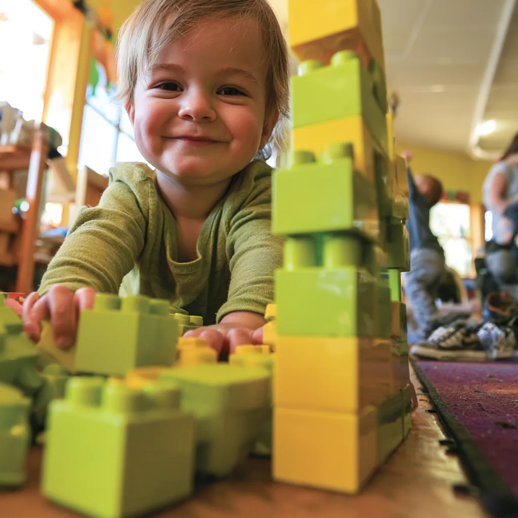 A toddler building a tower of green blocks