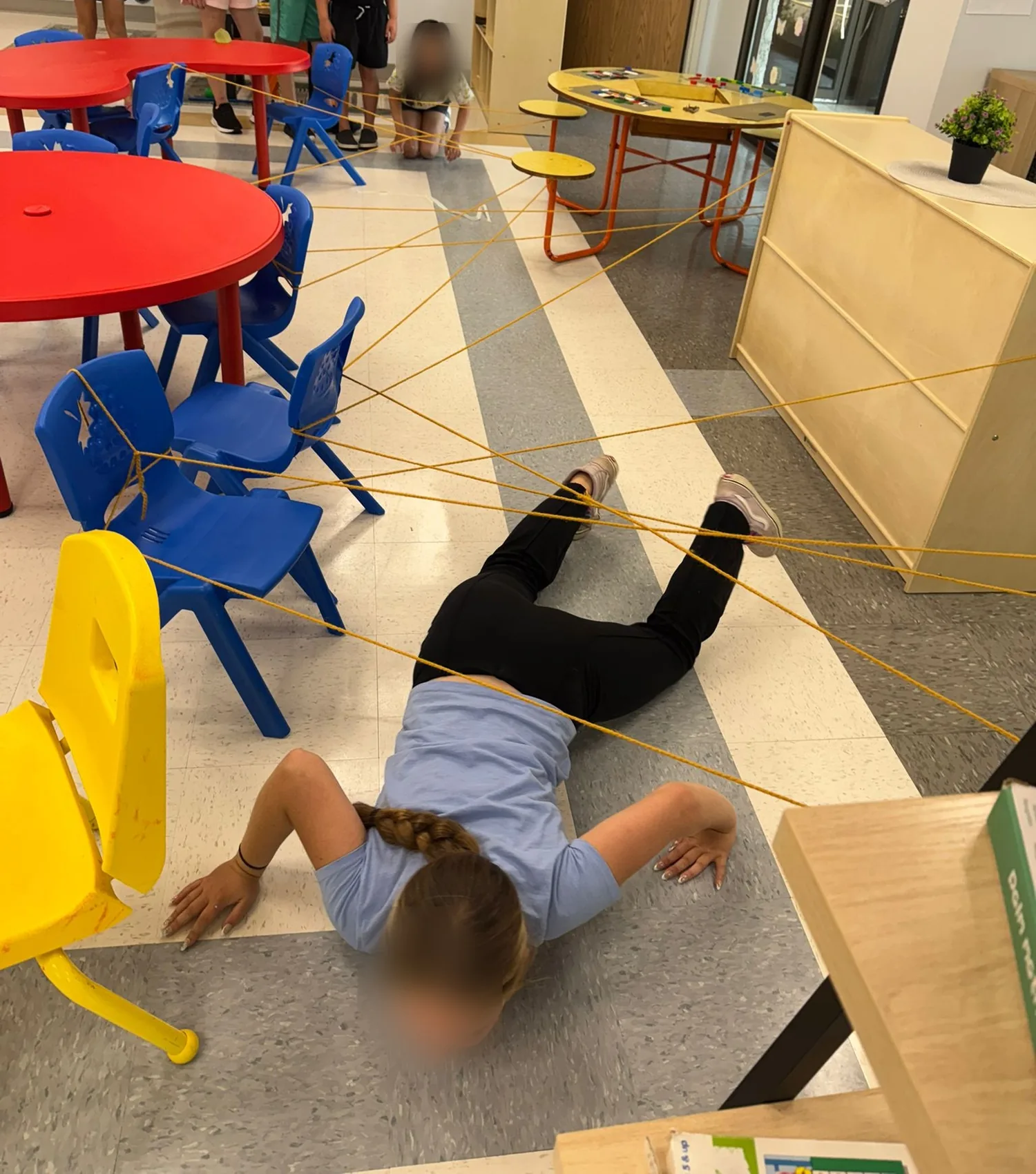 Children crawling through a yarn web strung between chairs
